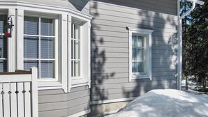 Une maison à l’extérieur grise, aux bordures blanches et dont la pelouse avant est recouverte de neige.