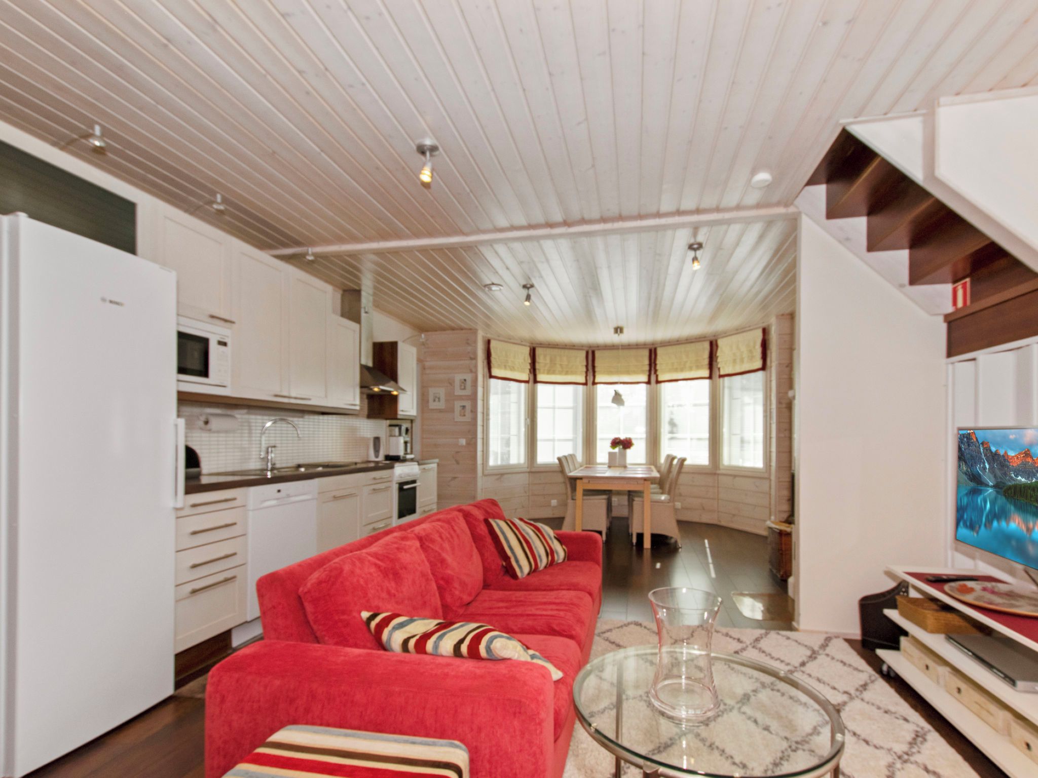 Una cocina moderna con armarios blancos, un sofá rojo y un comedor con mesa y sillas.