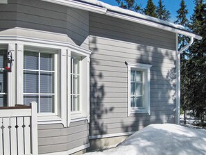 Une maison dotée d’une baie vitrée et d’une fenêtre plus petite, entourée de neige.
