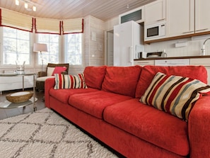 Un canapé rouge avec des coussins à rayures, une cuisine blanche avec un four à micro-ondes et un coin repas avec une table et des chaises.
