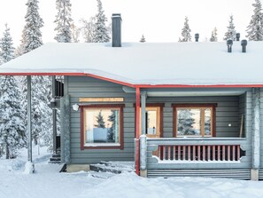 A wooden cabin with a porch, two windows, and a chimney.