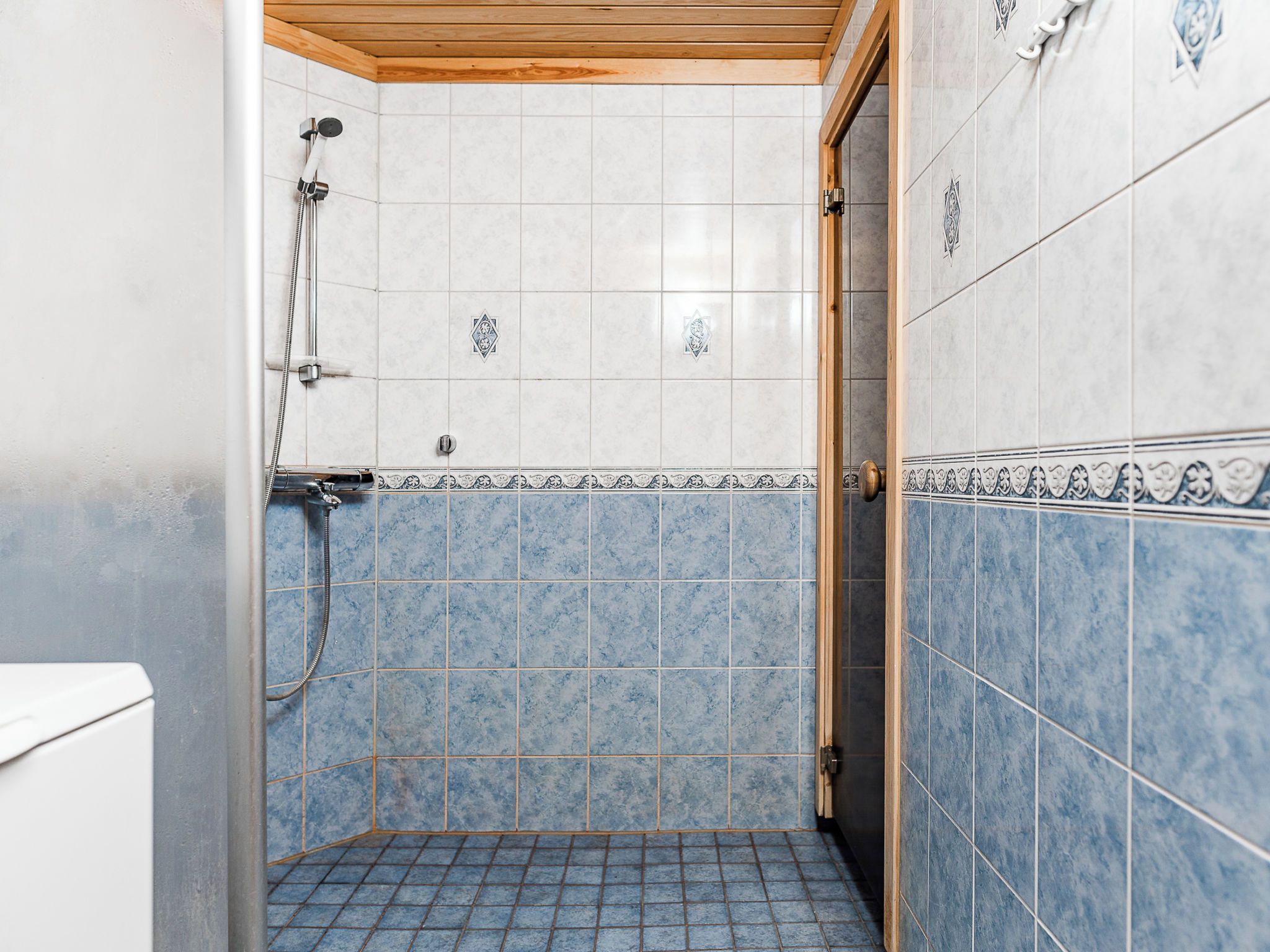 A small bathroom with a shower, tiled walls, and a wooden ceiling.