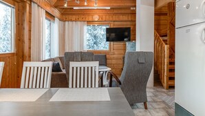 A cozy cabin interior with a dining area, seating, a television, and a kitchen area.