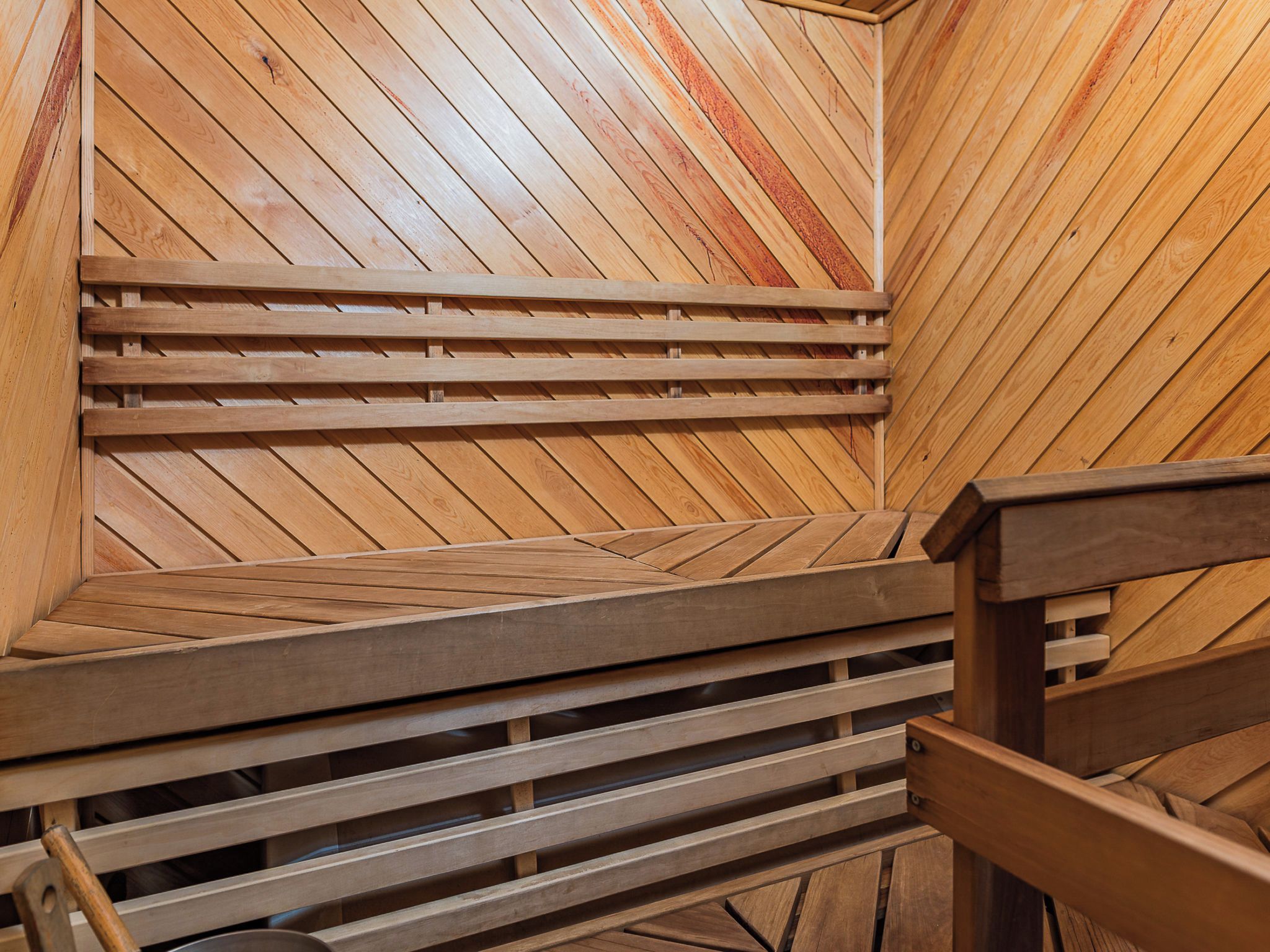 Un banco de sauna de madera con diseño de listones, frente a una pared de madera con patrón de espiga.