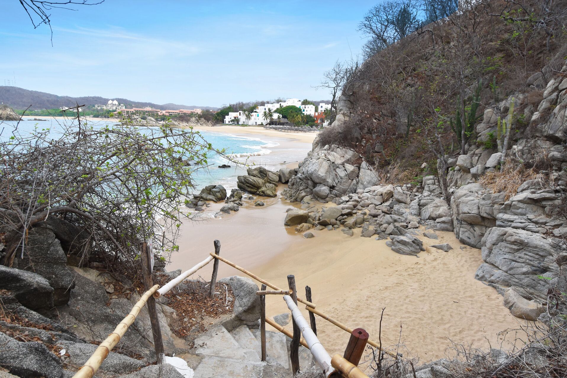 Una playa con terreno rocoso y una escalera de madera que baja hasta la orilla.