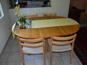 Un coin repas avec une table ronde en bois, quatre chaises, un vase rempli de fleurs jaunes et, au fond, une cuisine.