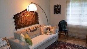 A living room with a sofa, a decorative headboard, a chair, a rug, and a window with blinds. - Hübeli (Arm) by Interhome (Zweisimmen)