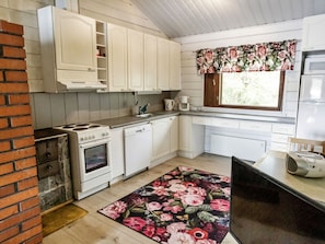 Une cuisine avec des meubles blancs, une cuisinière, un lave-vaisselle, une machine à café et une fenêtre agrémentée de rideaux à motifs floraux.