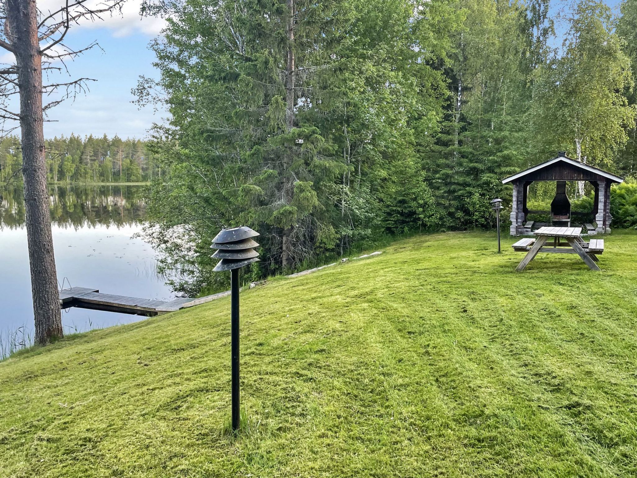 A grassy area with a gazebo and a dock extending into a lake, surrounded by trees.