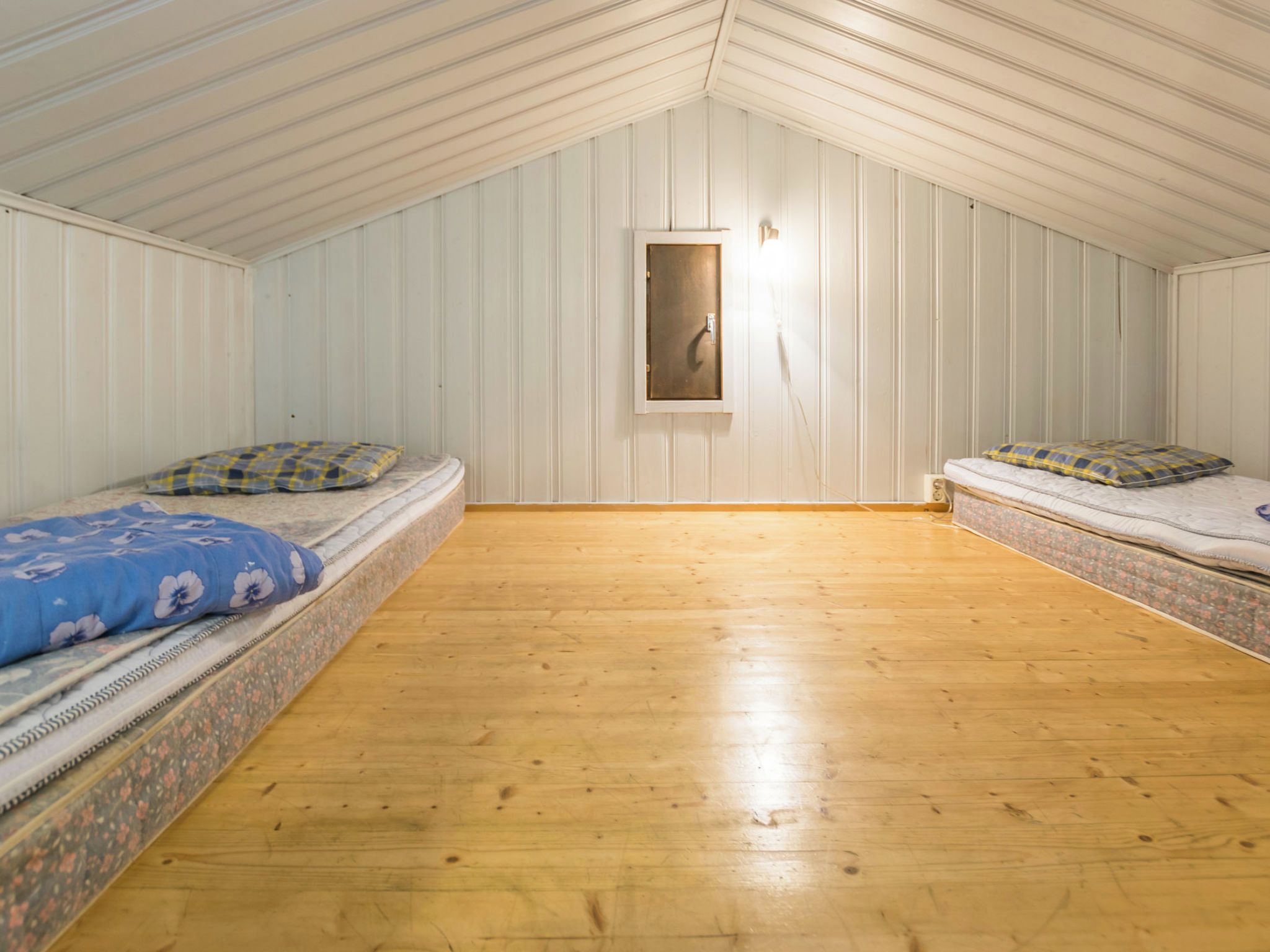 A room with two beds, wooden flooring, and white paneled walls.