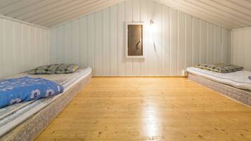 A room with two beds, wooden flooring, and white paneled walls.