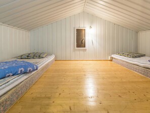 A room with two beds, wooden flooring, and white paneled walls.