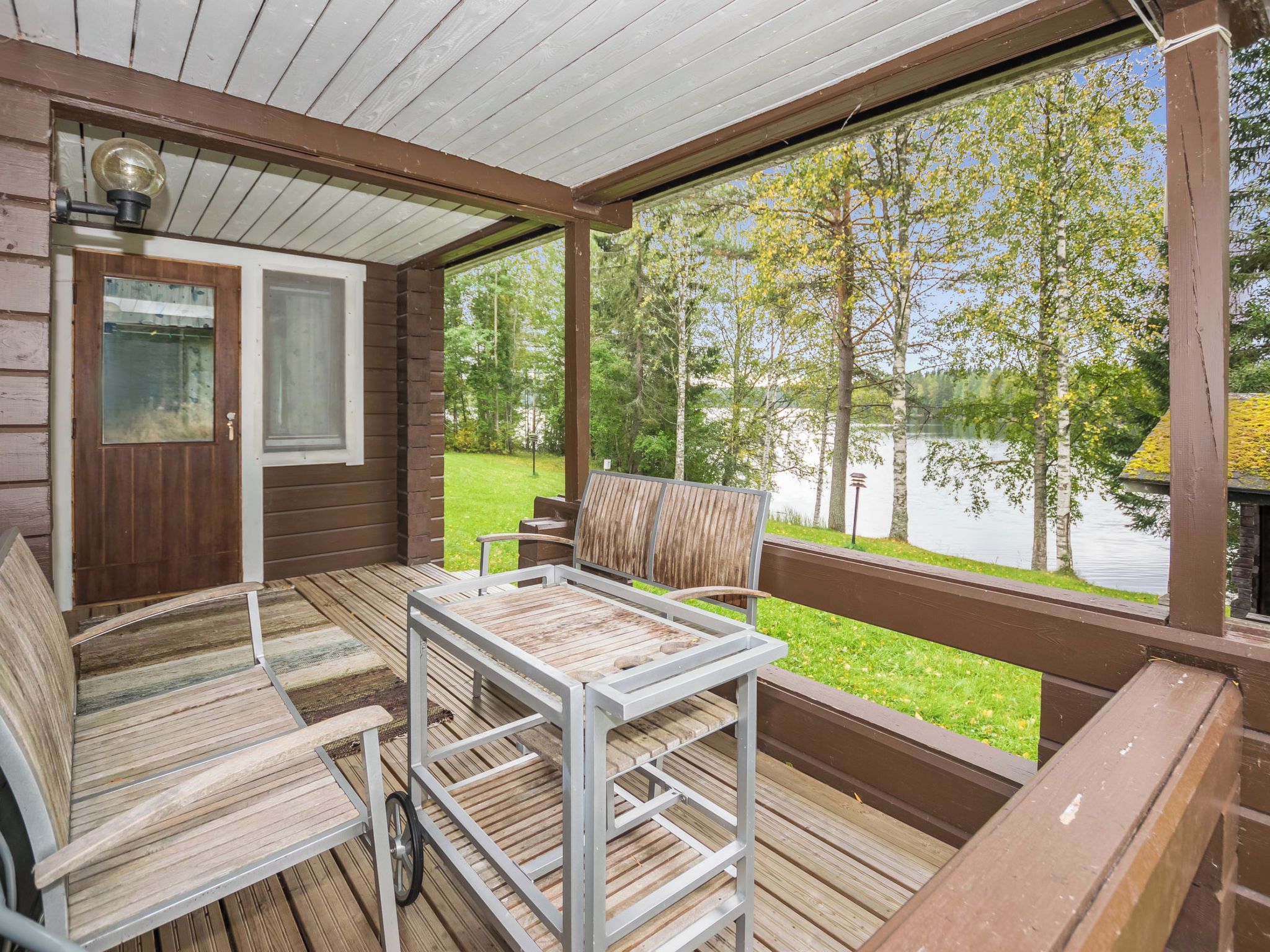 A covered deck with a table and chairs, overlooking a lake.