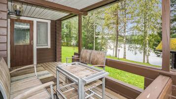 A covered deck with a table and chairs, overlooking a lake.