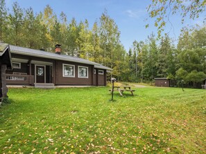 A cabin with a front porch, a picnic table, and a small shed in a wooded area. - Aurinkoranta by Interhome (Petäjävesi)