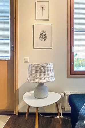 Een kamer met een witte lamp op een klein tafeltje, een deur met een raam en twee foto's in lijsten aan de muur.