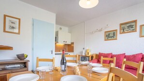 A dining area with a wooden table set for four, chairs, a bottle of wine, and a small kitchen in the background. - Lac du Lou 506 by Interhome (Val Thorens)