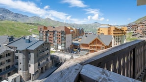 A modern hotel complex with multiple buildings, a wooden deck, and a mountainous backdrop. - Lac du Lou 506 by Interhome (Val Thorens)
