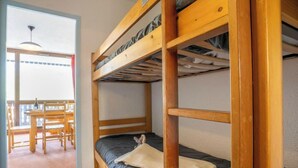A bunk bed room with a wooden frame, a table, chairs, and a view of the outside. - Lac du Lou 506 by Interhome (Val Thorens)