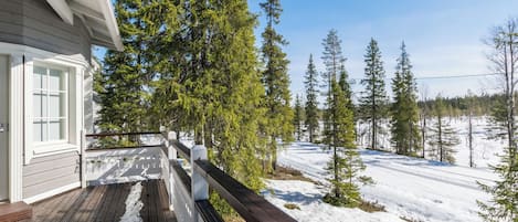 Una terraza de madera con barandilla que da a un paisaje nevado con árboles.