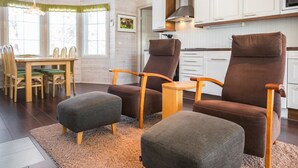 Ein gemütliches Wohnzimmer mit einem Holzesstisch, zwei braunen Sesseln und einem grauen Hocker.