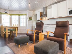 Une cuisine moderne avec des armoires blanches, un four à micro-ondes et une cuisinière. On y trouve deux chaises marron avec des accoudoirs en bois et une petite table. Une table à manger avec des chaises est visible au fond.
