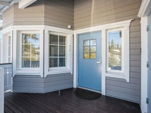 Un petit hall d’entrée avec une porte bleue, des moulures blanches et une terrasse en bois foncé.