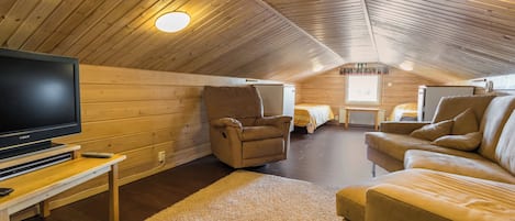 Une pièce mansardée chaleureuse avec un plafond en bois, un téléviseur à écran plat, un canapé, un fauteuil et une petite table.