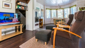 Ein gemütliches Wohnzimmer mit einer Holztreppe, einem Fernseher, einem Essbereich und einem Bücherregal.
