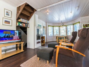 Un salon confortable avec un téléviseur, des étagères à livres, un escalier et un coin repas.