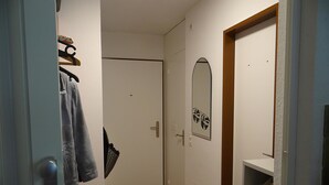 Un pasillo con una puerta, un perchero, un espejo y una estantería con objetos.