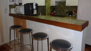 Una cocina con cafetera, microondas y tostadora. Hay tres taburetes frente a la encimera.