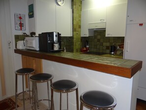 Una cucina con una macchina da caffè, un forno a microonde e un tostapane. Ci sono tre sgabelli davanti al bancone.