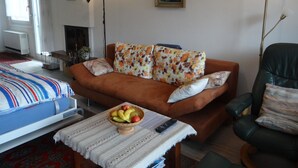 Una sala de estar con un sofá, una mesa de centro con fruta, una chimenea y una cama con manta a rayas.