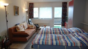 Un dormitorio con cama, sofá, sillón, escritorio, lámpara y ventana con cortinas.