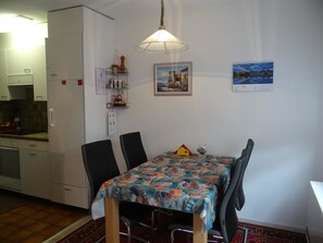 Une cuisine de taille réduite avec des meubles blancs, une table à manger avec des chaises et un luminaire suspendu.