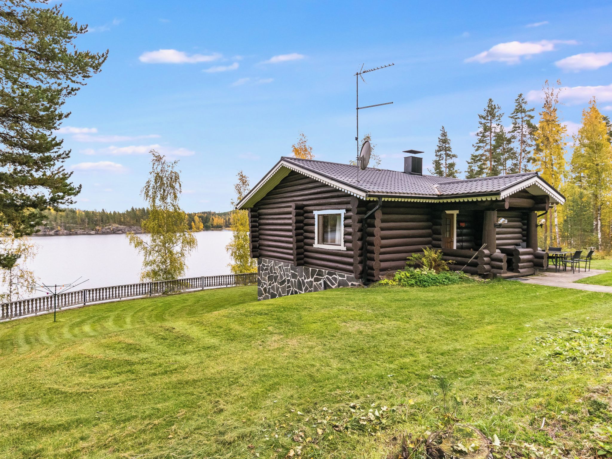 A log cabin with a stone foundation, a small porch, and a view of a lake.