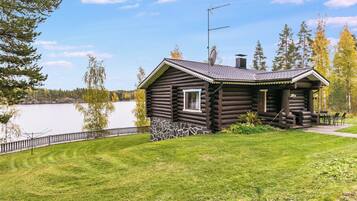 A log cabin with a stone foundation, a small porch, and a view of a lake.