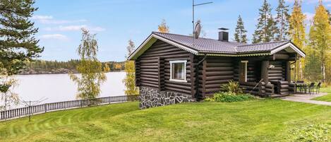 A log cabin with a stone foundation, a small porch, and a view of a lake.