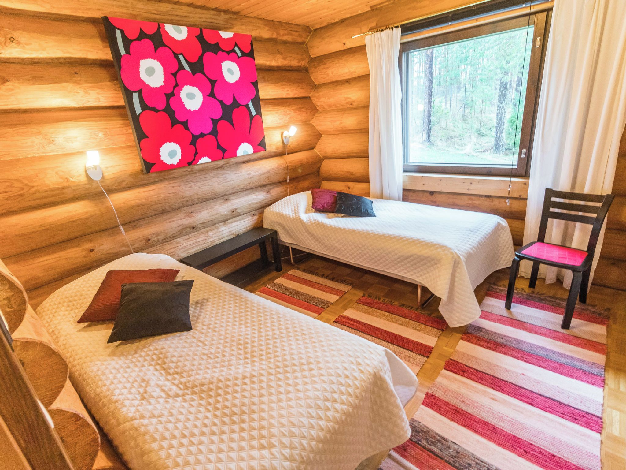 Une chambre de style rustique avec deux lits, une chaise, une fenêtre avec des rideaux et un mur orné d’un motif floral.