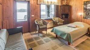 Une chambre à coucher située dans une cabane en bois, comprenant un lit, deux fauteuils en osier, un banc, une fenêtre donnant sur un lac et une armoire en bois.