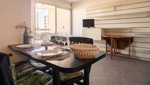 A dining area with a table set for two, a television mounted on the wall, and a window providing natural light. - Ipanema Sud by Interhome (Canet-Plage)