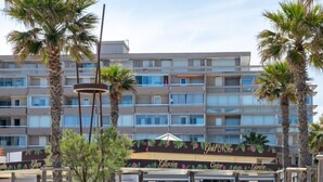 A multi-story hotel with balconies, a covered outdoor seating area, and palm trees. - Ipanema Sud by Interhome (Canet-Plage)