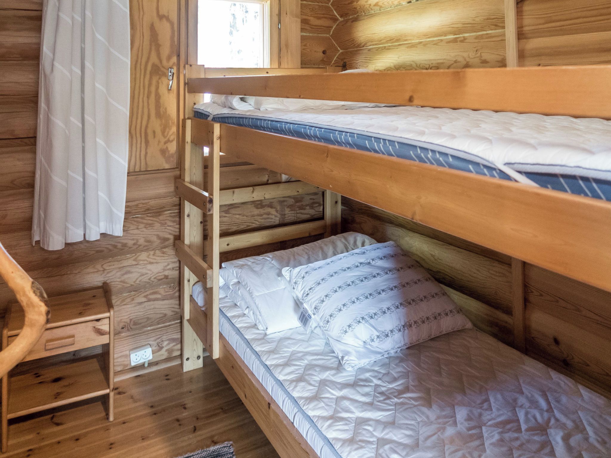 A bunk bed with a wooden ladder, a small table, and a window with curtains.