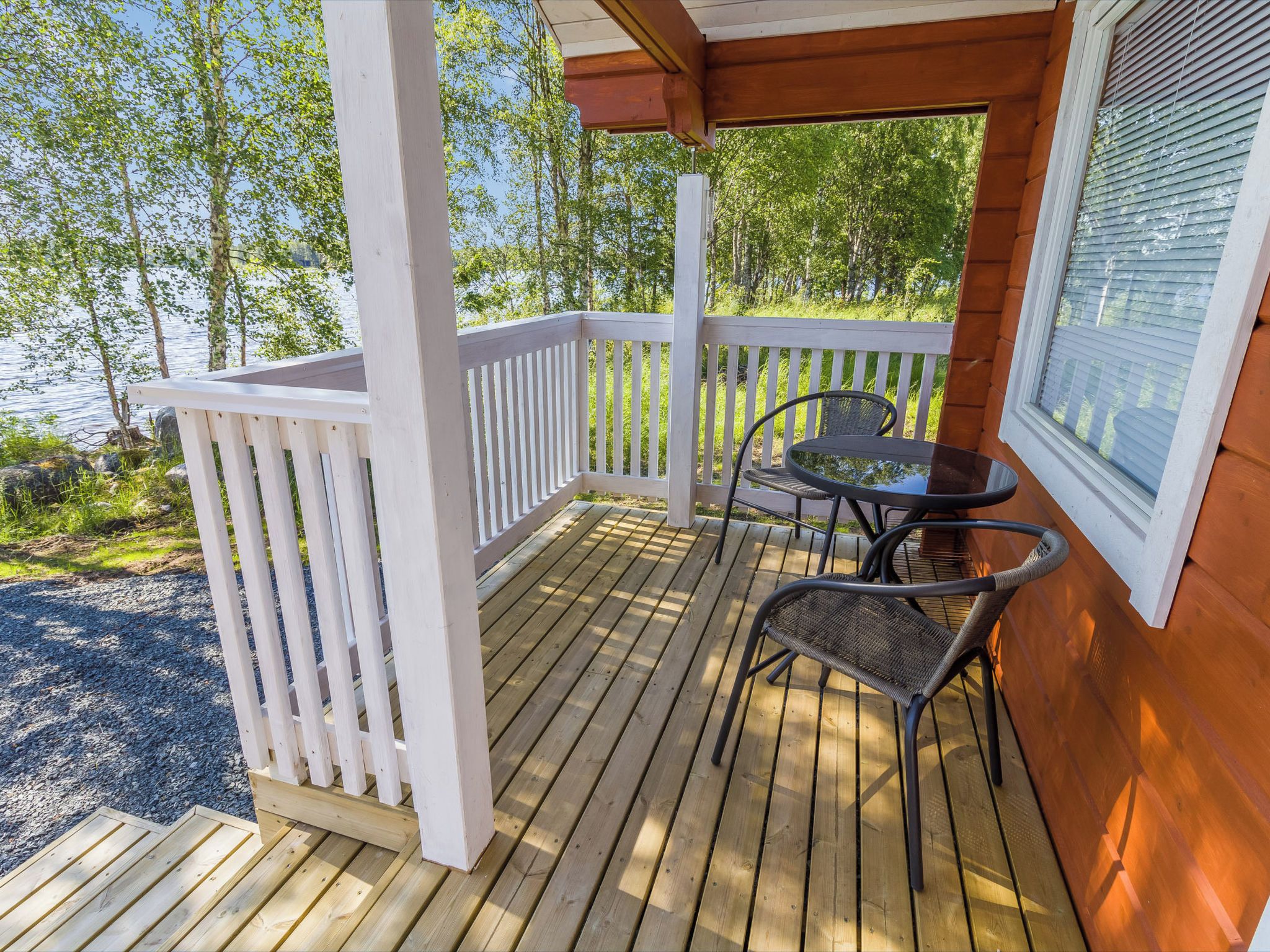 A wooden deck with a white railing, two chairs, and a table.