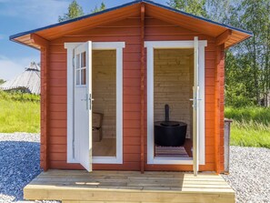A small wooden cabin with two open doors, a fireplace, and a wooden deck.