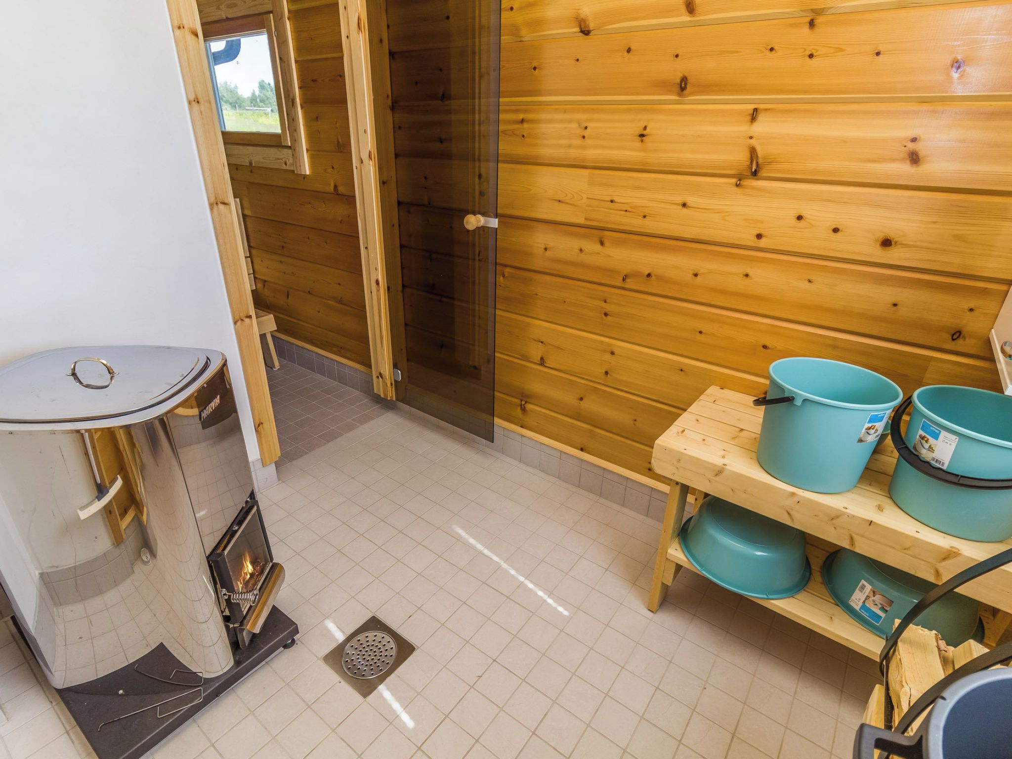 Interno di una baita in legno con sauna, lavandino e ripiano con secchi blu.