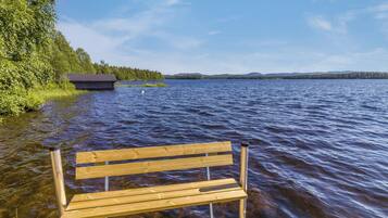 A wooden bench by a lake with a cabin in the background.