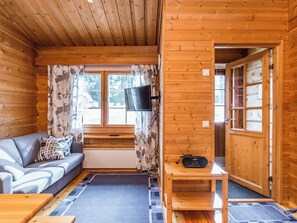 Tunnelmallinen mökin sisustus, jossa on sohva, seinälle asennettu televisio ja pienellä pöydällä oleva radio.