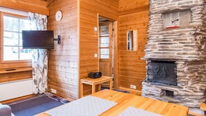 A cozy cabin interior with wooden walls, a stone fireplace, a television mounted on the wall, and a window with curtains. - Rukansyli 1 by Interhome (Kuusamo)